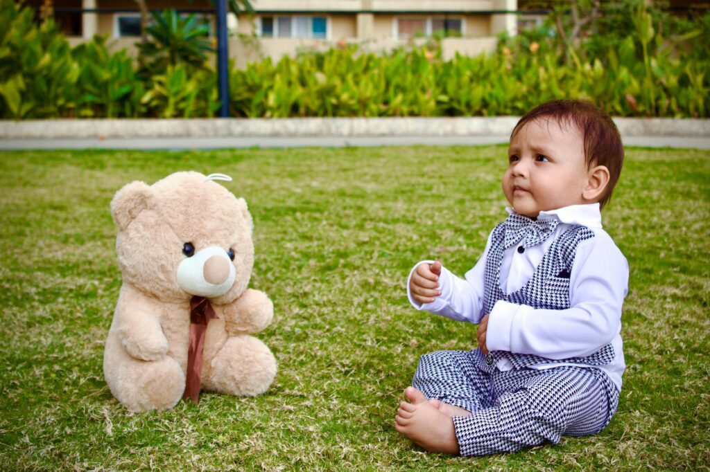 baby boy sitting with a teddy bear on a lawn